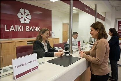 A Laiki Bank teller serving a client at the branch counter, beneath the LAIKI BANK sign